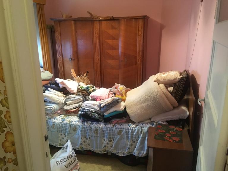 Voor de ontruiming: Slaapkamer met bed, waar dekens en kledij opgehoopt liggen