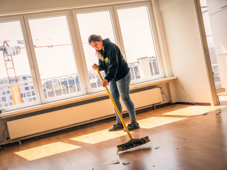 werknemer met bezem in leeg appartement
